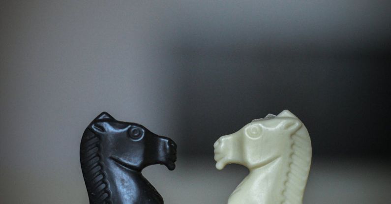 Puzzle Board Games - Closeup of black and white figures of knight standing in front of each other on chessboard square