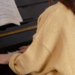 Solo Play - Back view of anonymous female pianist practicing piano while sitting on stool in light room with white walls