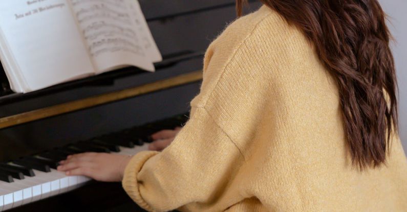 Solo Play - Back view of anonymous female pianist practicing piano while sitting on stool in light room with white walls