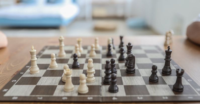 Collectible Board Games - Small white and black figurines on thin square chess board in bedroom in daytime on blurred background