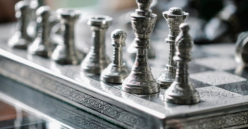 Strategy Board Games - Classic metal chess board with set figurines designed with carved ornaments and placed on glass table in light room